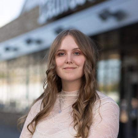 Photograph of a woman in focus wearing a light sweater.