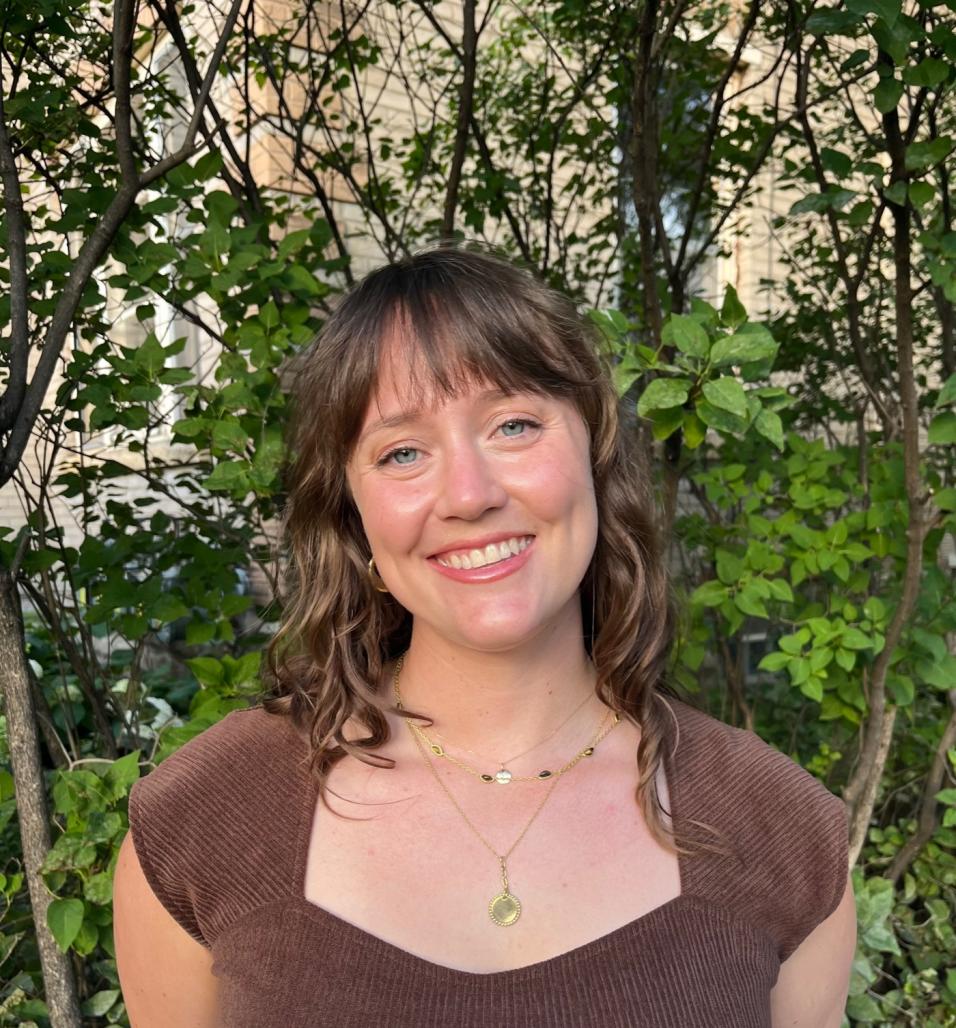 Photograph of Lucy Rea from the chest up in front of foliage.