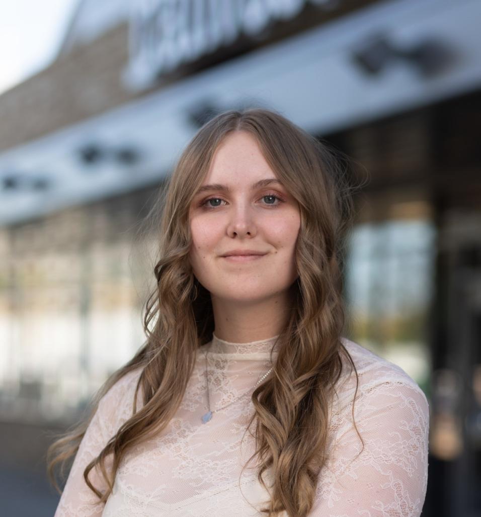 Photograph of a woman in focus wearing a light sweater.